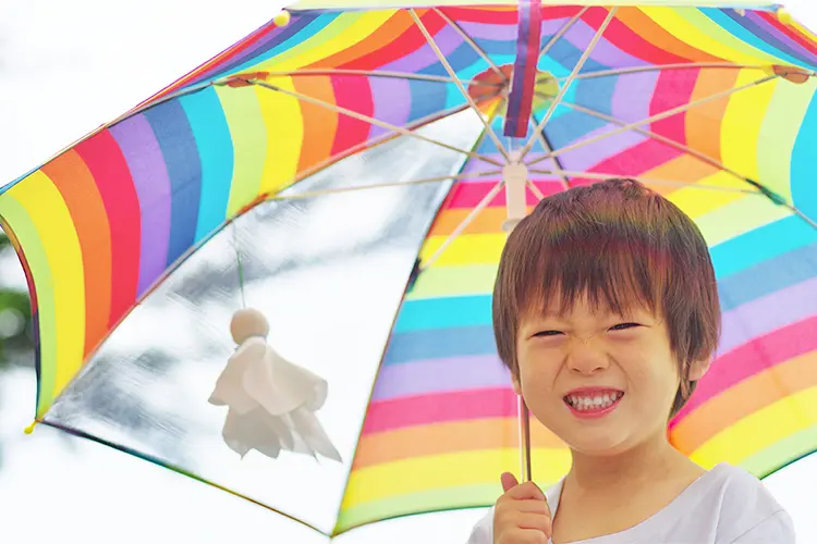 てるてる坊主をつけた傘を持つ雨の中でも楽しそうな笑顔の子供